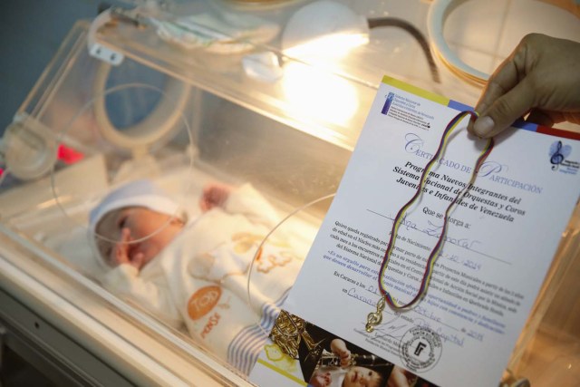 A nurse holds a certificate of membership from "El Sistema", as part of its "New Members" program, next to a newborn baby at a public maternity hospital in Caracas
