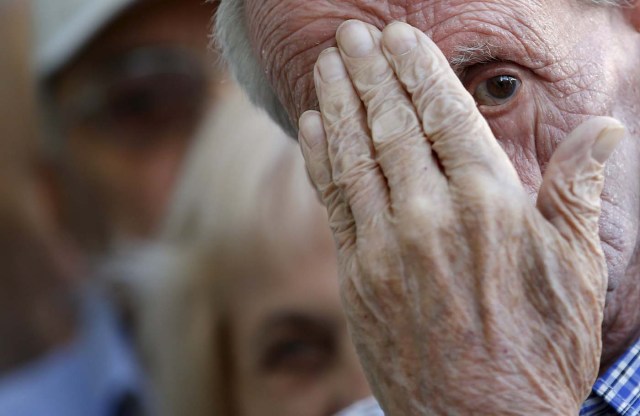 Pensioners wait in front of the main entrance of a National Bank branch to receive part of their pensions in central Athens