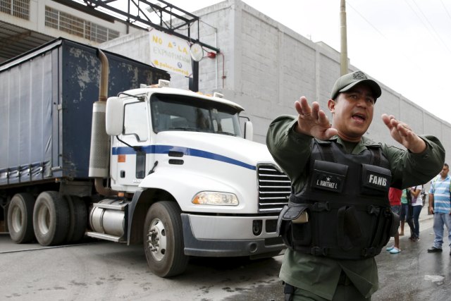 A Venezuelan National Guard walks in front of a truck as it leaves the facility used by Empresas Polar as a distribution center, while company employees shout inside, during the occupation of its installations by government representatives in Caracas July 30, 2015. REUTERS/Carlos Garcia Rawlins