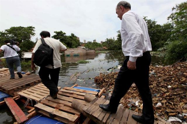 Fotografía del 29 de diciembre de 2015, del intendente de Asunción (Paraguay), Mario Ferreiro (d), mientras cruza un puente flotante construido por pobladores de un barrio en Asunción. No es el puente de Londres ni el mítico Kwai, pero la modesta estructura flotante construida por unos estudiantes de arquitectura en el barrio de la Chacarita, en Asunción, se ha convertido en un símbolo de solidaridad con los miles de personas que sufren las inundaciones del río Paraguay. Hasta la fecha hay unos 100.000 evacuados por la crecida del río, que ha golpeado principalmente a los vecindarios de Asunción ubicados en sus márgenes fluviales, como el de Ricardo Brugada, conocida popularmente como la Chacarita. EFE/Andrés Cristaldo Benítez