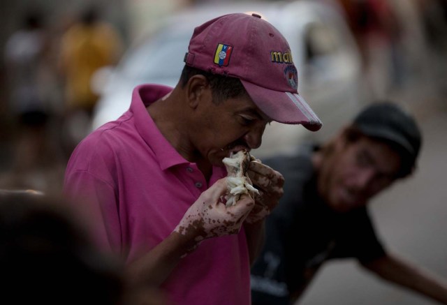 En esta foto del 2 de junio de 2016, un hombre come una guanábana que recogió de la basura frente a un supermercado en el centro de Caracas, Venezuela. Gente que se considera de clase media, aunque su nivel de vida se ha derrumbado debido a la inflación galopante, la escasez de alimentos y la caída de la moneda salen a las calles a revolver en la basura en busca de algo para comer. (AP Foto/Fernando Llano)