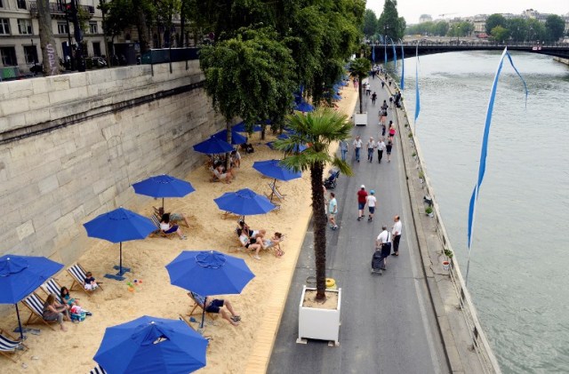 A picture taken on the bank of the Seine river, in central Paris, on July 20, 2016 shows people relaxing under parasols in "Paris Plage" (Paris Beach) during the opening day of the event. The 15th edition of Paris Plage will run until September 4, 2016. / AFP PHOTO / BERTRAND GUAY