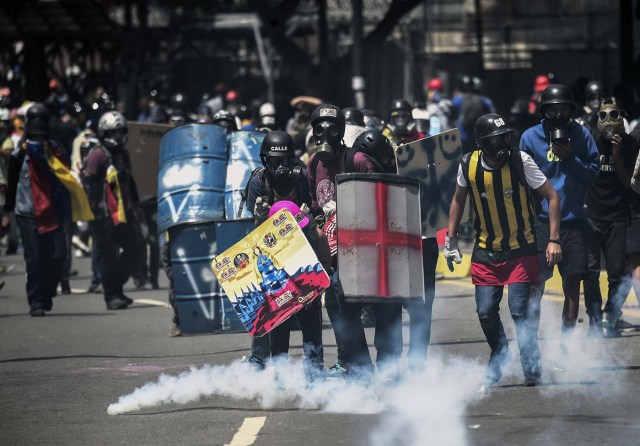 Opposition activists using gas masks and makeshift shields clash with riot police during an anti-government protest in Caracas, on June 22, 2017. / AFP PHOTO / JUAN BARRETO