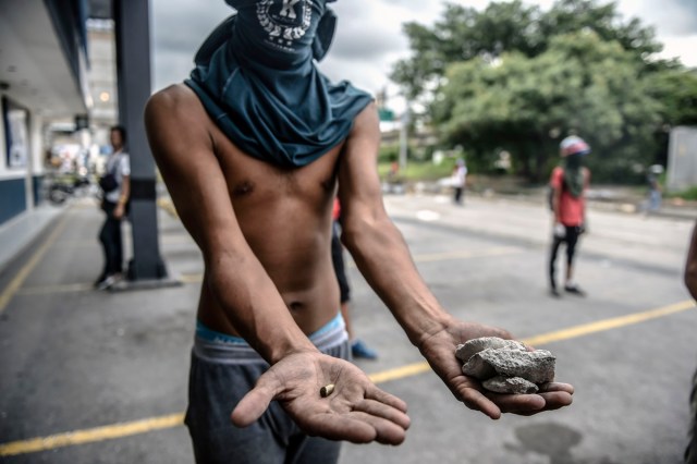 An opposition demonstrator shows a bullet fired by riot police and stones thrown by demonstrators during clashes in an anti-government protest in Caracas, on July 20, 2017. A 24-hour nationwide strike got underway in Venezuela Thursday, in a bid by the opposition to increase pressure on beleaguered leftist President Nicolas Maduro following four months of deadly street demonstrations. / AFP PHOTO / JUAN BARRETO
