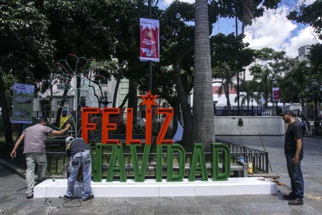 Men work on the installation of a christmas sign in Caracas on November 2, 2017. Venezuela will put into circulation a new bank note of 100,000 Bolivars, which multiplies by five the current largest denomination, and will move towards the massive use of electronic money to avoid what President Nicolas Maduro calls the "bank note war". / AFP PHOTO / JUAN BARRETO