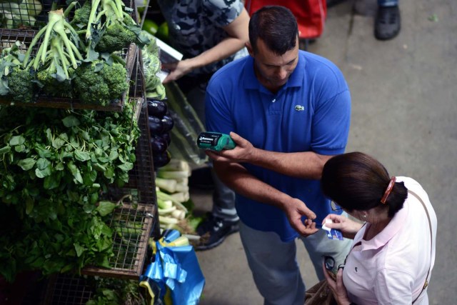 A woman pays for groceries at the municipal market of Chacao in Caracas on November 2, 2017. This week, Venezuelan President Nicolas Maduro introduced a new bank note of 100,000 Bolivars - five times the current largest denomination - and announced a 30 percent minimum wage hike. / AFP PHOTO / FEDERICO PARRA