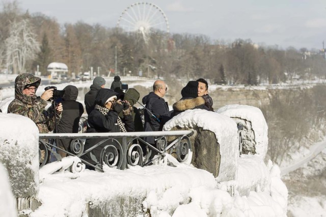 Tourists take photos of the Horseshoe Falls in Niagara Falls, Ontario on January 3, 2018. The cold snap which has gripped much of Canada and the United States has nearly frozen over the American side of the falls. / AFP PHOTO / Geoff Robins