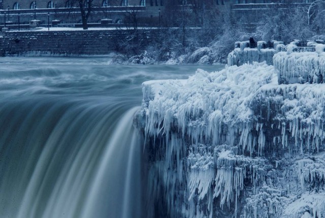 A lone visitor takes a picture near the brink of the ice covered Horseshoe Falls in Niagara Falls, Ontario, Canada, January 3, 2018. REUTERS/Aaron Lynett