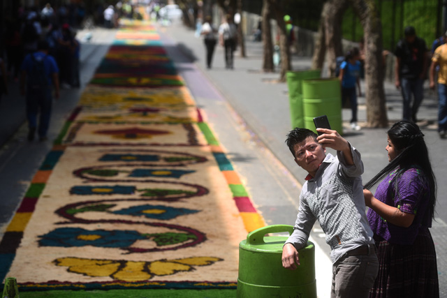 GU4005. CIUDAD DE GUATEMALA (GUATEMALA), 29/03/2018.- Una pareja se toma fotos frente a una alfombra de serrín hoy, jueves 29 de marzo de 2018, durante la celebración del Jueves Santo en Ciudad de Guatemala (Guatemala). Miles de guatemaltecos se reunieron este Jueves Santo para elaborar una alfombra de serrín, considerada la más grande del mundo, en el Paseo de la Sexta, la calle peatonal más emblemática del centro histórico de la capital. Los 1.200 voluntarios, convocados por la Municipalidad metropolitana, empezaron hoy a hacer esta alfombra de más de 2.000 metros de longitud y en la que se emplearon un millar de sacos de serrín. EFE/Edwin Bercían