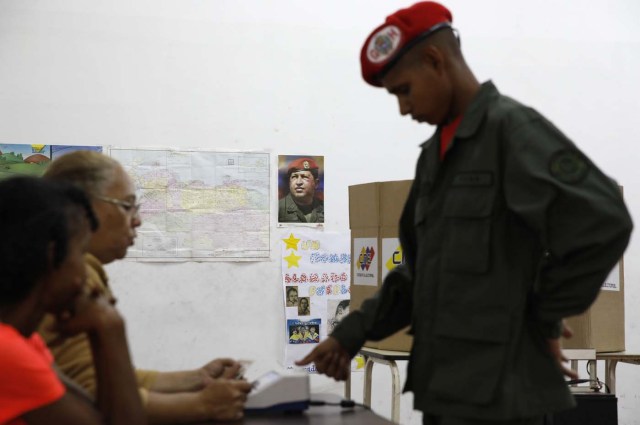 With an image of the late Venezuelan President Hugo Chavez on the wall a Venezuelan soldier marks his thumb print as he prepares to cast his vote at a polling station during the presidential election in Caracas, Venezuela, May 20, 2018. REUTERS/Carlos Garcia Rawlins