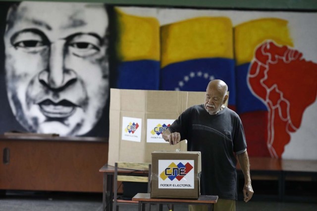 With an image of the late Venezuelan President Hugo Chavez behind him a Venezuelan citizen casts his vote at a polling station during the presidential election in Caracas, Venezuela, May 20, 2018. REUTERS/Marco Bello